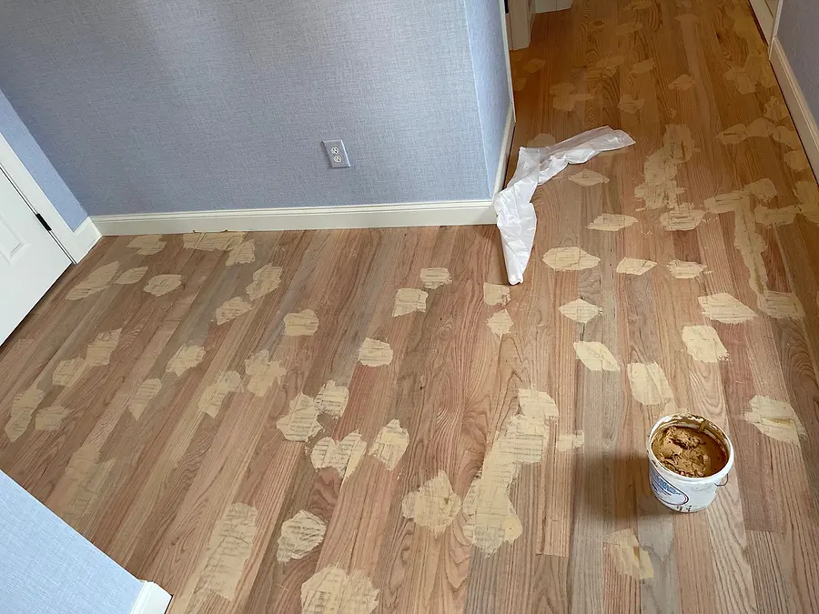 Hardwood floor with wood filler spread over gaps and nail holes before final sanding